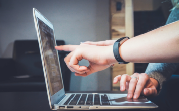 Two people pointing at a laptop screen discussing the benefits of implementing proposal automation solutions.